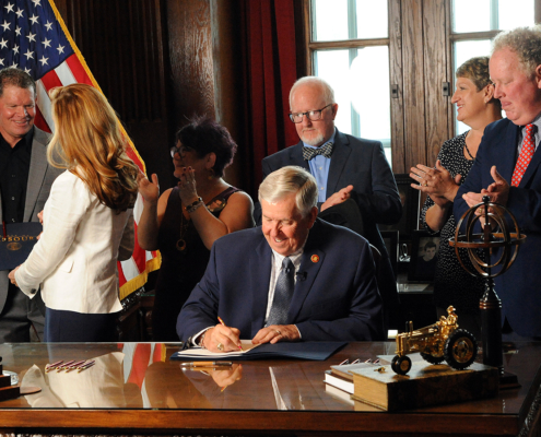 Governor Parson signs a bill into law Monday creating a statewide drug monitoring program. Coach Jim Marshall, left, receives the first signed copy of the bill in honor of his son, Cody. Photo by Shaun Zimmerman