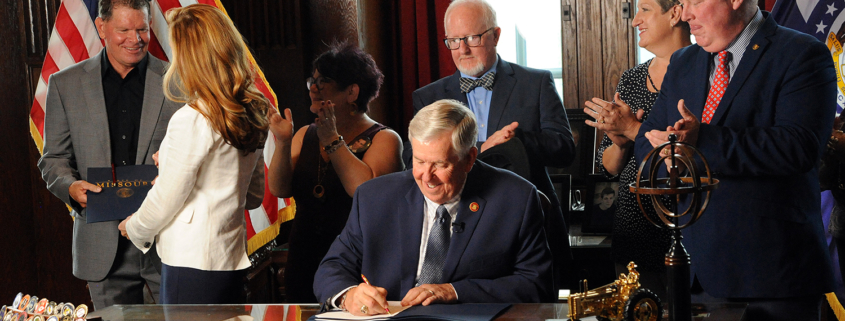Governor Parson signs a bill into law Monday creating a statewide drug monitoring program. Coach Jim Marshall, left, receives the first signed copy of the bill in honor of his son, Cody. Photo by Shaun Zimmerman